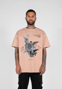 Lyserød bomulds t-shirt med grafisk tryk af en engel og en figur, med sorte og blå accenter. Korte ærmer og afslappet pasform.