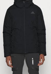 Svart vadderad jacka med hög krage, framzipper och sidofickor. Har Adidas-logga i grått och texturerad yta.