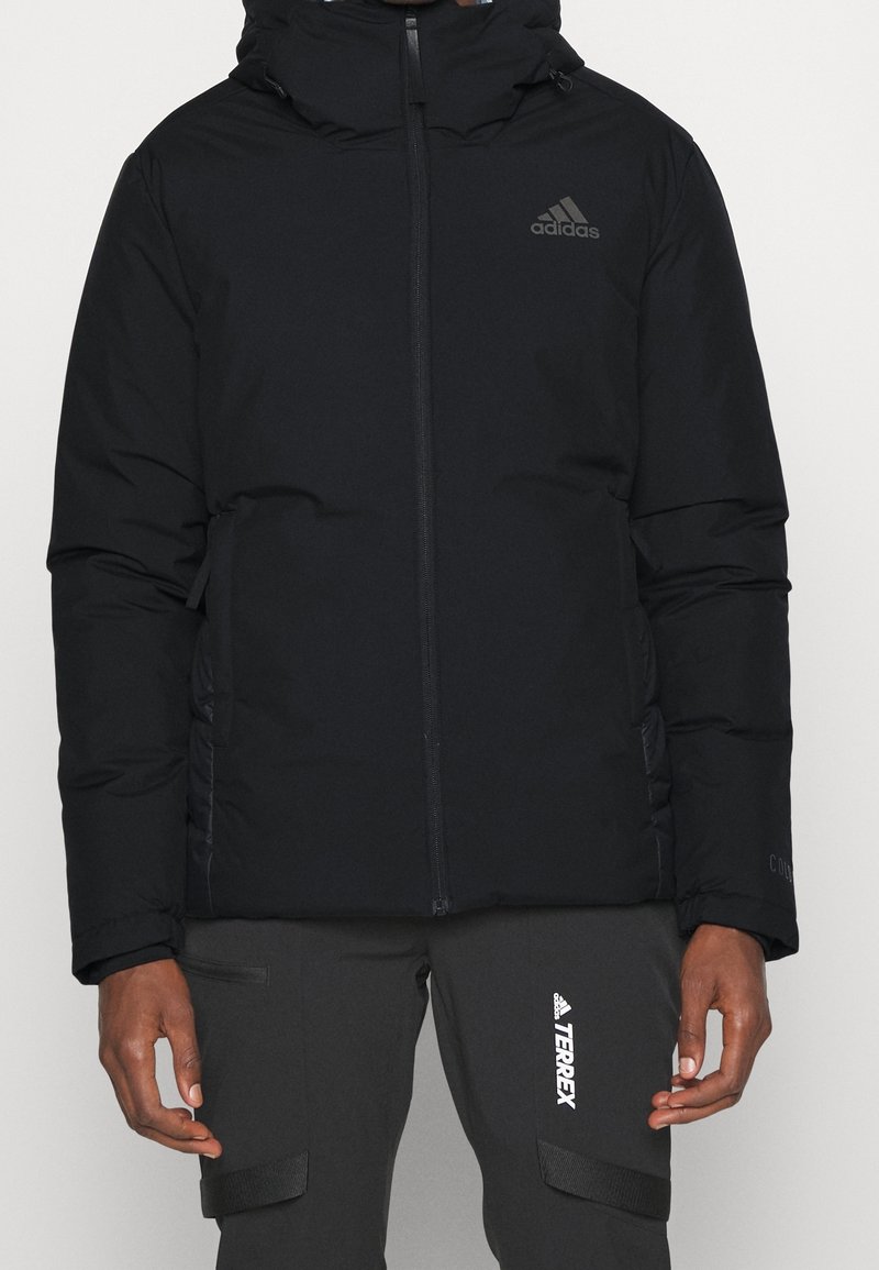 Svart vadderad jacka med hög krage, framzipper och sidofickor. Har Adidas-logga i grått och texturerad yta.