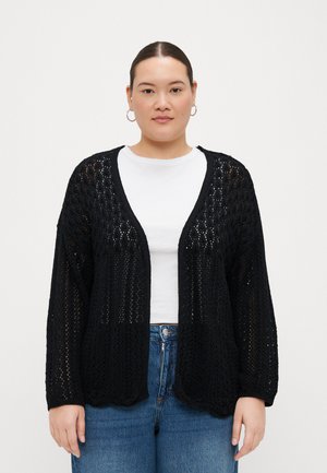 Black open-front cardigan made from textured, knit material. Features wide sleeves and a relaxed fit, layered over a white t-shirt and jeans.