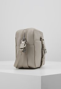 Beżowa skórzana torebka na ramię o prostokątnym kształcie, z zamknięciem na zamek błyskawiczny u góry, regulowanym paskiem oraz akcentami w srebrnym odcieniu.