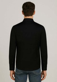 Camicia nera a maniche lunghe con colletto, realizzata in tessuto morbido. Presenta polsini con bottoni e un orlo curvo. Indossata con jeans in denim blu.