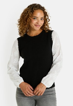 Un pull en tricot sans manches noir avec un col côtelé, associé à une blouse blanche à manches longues ornée de motifs floraux brodés.