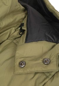 Binnenkant van een olijfgroene jas met textuurstof, een zwarte voering en zilveren metalen drukknopdetails met een ritsaanhanger.