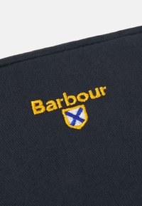 Námořnická tkanina s žlutě vyšitým textem "Barbour" a šikmým logem s modrým a bílým designem, rovnoměrně strukturovaná.