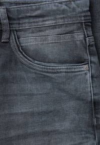 Jean en denim foncé avec une texture lisse, une poche avant avec un détail de couture et un petit rivet en métal près du bord de la poche.