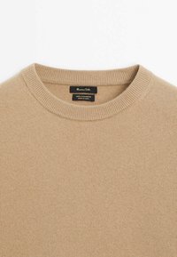 Pull beige à col rond en 100 % cachemire avec col côtelé et étiquette de marque noire à l'intérieur de l'encolure.