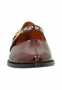 Chaussure plate en cuir laqué bordeaux avec un bout arrondi, présentant une sangle à boucle dorée et des œillets décoratifs dorés le long du cou-de-pied.
