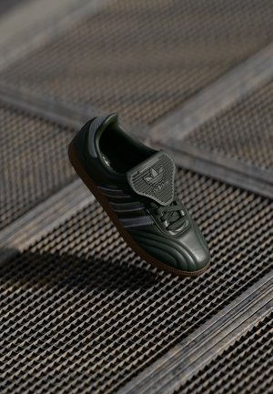 Green leather sneaker with silver stripes, textured toe cap, and a padded tongue. Rubber sole offers traction. Classic design elements are present.