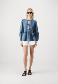 Zila svītrainā blūze ar caurumu priekšpusē, pūkainām piedurknēm un pieguļošu jostasvietu. Apvienota ar baltām saplēstām šortiem un melniem atklātiem zābakiem.