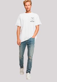 Weißes Baumwoll-T-Shirt mit dem Grafikdesign "WEISER VATER" und einer Buchillustration, kombiniert mit hellblauen, ausgewaschenen Jeans und weißen Sneakern.