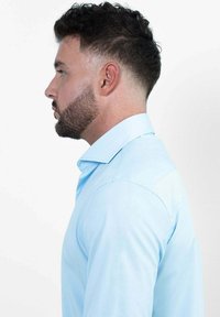 Lichtblauw overhemd met een puntig kraag en lange mouwen, met een gladde textuur en een getailleerd ontwerp, zijwaarts bekeken.