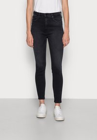 Jeans ajustados en denim oscuro, con una cintura alta, diseño de cinco bolsillos y detalles de costura sutiles. Combinados con zapatillas blancas.