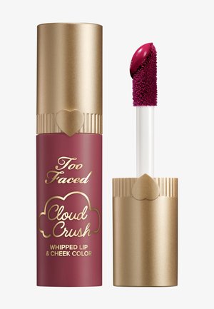 Tube de couleur pour les lèvres et les joues maroon et or avec un capuchon doré à design strié et un accent en forme de cœur, accompagné d'un applicateur blanc.