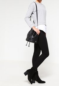 Felpa grigia a maniche lunghe indossata sopra una camicia bianca, jeans skinny neri, stivaletti neri con tacco e una borsa a secchiello nera con dettagli in occhio di pernice.