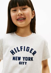 Szara koszulka z krótkim rękawem z granatowym wyszywanym napisem "HILFIGER NEW YORK CITY", z okrągłym dekoltem i luźnym krojem.