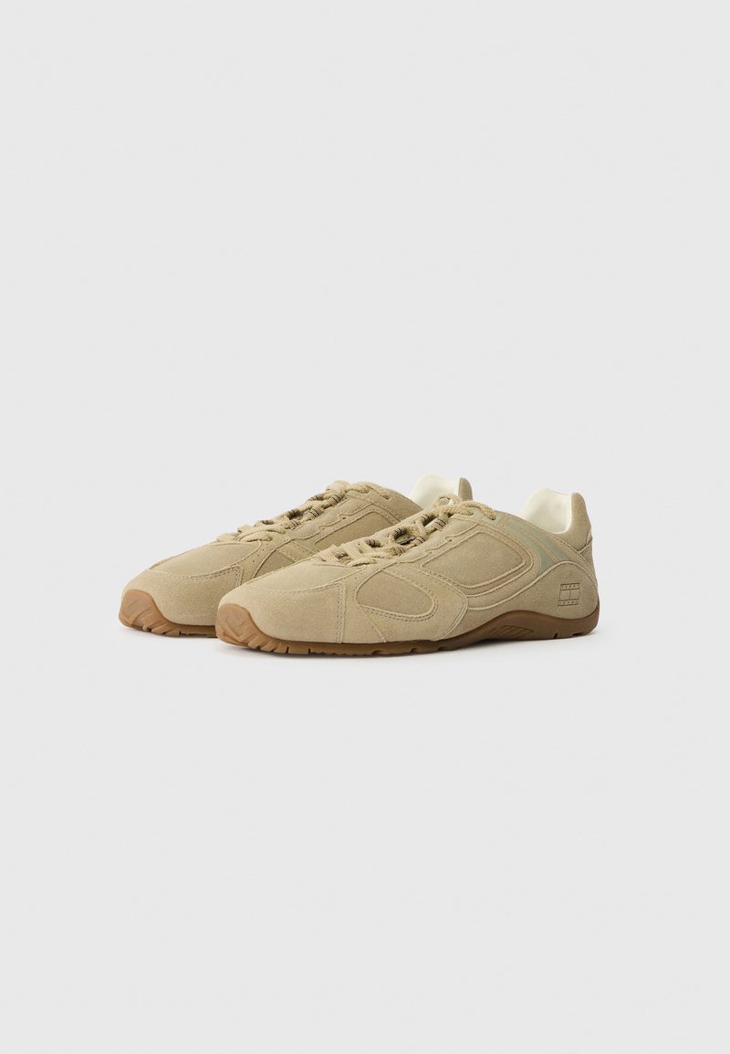 Beige athletic shoes made of suede, featuring a textured surface, rubber sole, and lace-up design with subtle branding on the side.