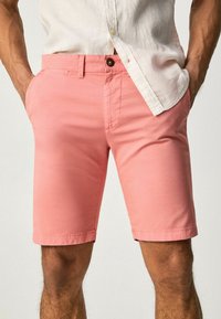 Męskie szorty w jasnoróżowym kolorze, wykonane z gładkiego materiału, z kieszeniami z przodu i zapięciem na guzik, zaprojektowane do noszenia na co dzień.