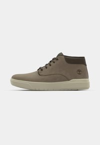 Bruine suède mid-top schoenen met donkerbruine accenten, ronde neus, vetersluiting aan de voorkant en een lichtgekleurde rubberen zool. Bevat logo aan de zijkant.
