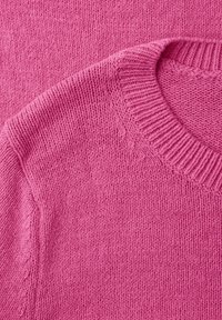 Gros plan sur un tissu tricoté rose doux avec un col rond côtelé et une texture de tricot visible.