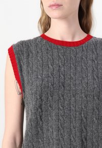 Pull en tricot gris avec un design en câble texturé, un col et des emmanchures ribbed rouges, des manches courtes et une silhouette ajustée.