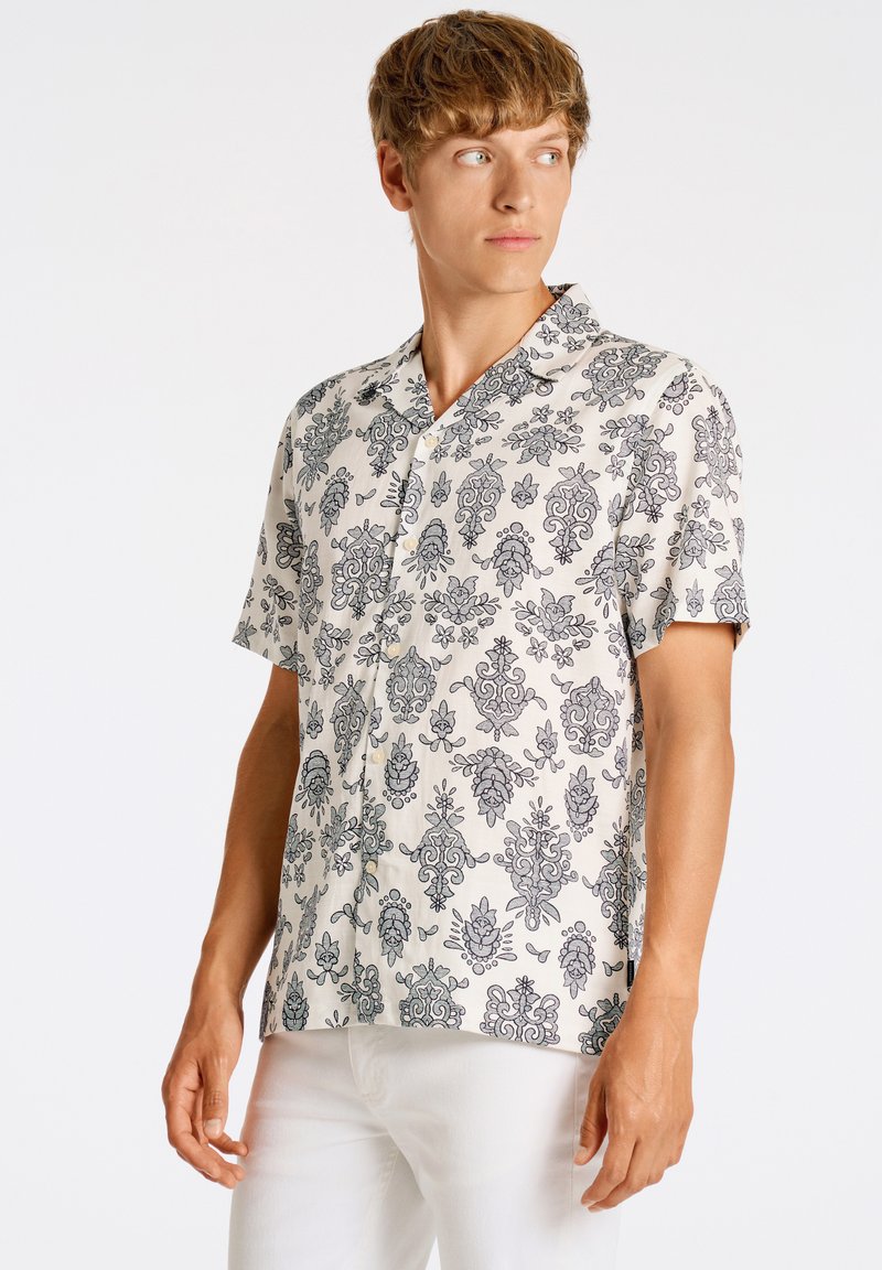 Camisa de manga corta en tejido ligero con un patrón floral negro sobre un fondo beige, con cuello y diseño de botonera frontal.