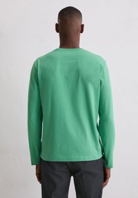 Koszulka z długim rękawem z zielonej bawełny o jednolitym kolorze, z klasycznym okrągłym dekoltem i luźnym krojem, o gładkiej fakturze i prostej konstrukcji.