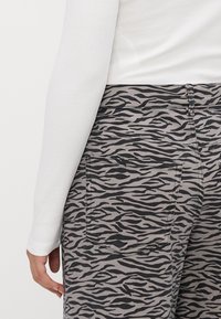 Jean gris avec un motif et un design de rayures de tigre noires, dotés de poches arrière et d'une ceinture, associés à un haut à manches longues blanc.