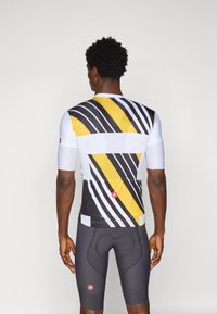 Korte ermer sykkeltrøye med hvite, gule og svarte skråstriper. Laget av et teksturert, pustende materiale med en tettsittende design.