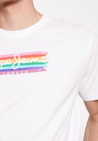 Camiseta de algodón blanca de manga corta con un logo colorido de pinceladas en rosa, naranja, verde y azul, que dice "Pepe Jeans London."