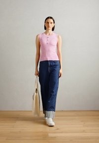 Rosa ribbet tanktopp uten ermer med knappedetaljer, kombinert med løse blå denimjeans. Modellen bærer en beige totebag og har på seg hvite sneakers.