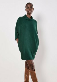 Abito tunica lavorato a maglia verde con colletto alto, maniche corte e una vestibilità ampia e rilassata. Presenta tasche laterali e un motivo testurizzato.