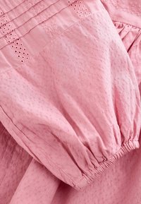 Lys rosa bomuldsbluse med struktureret stof, broderede blomsterdetaljer og elastiske manchetter. Den har et afslappet, samlet design.