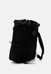 Mochila negra con cordón, hecha de un tejido duradero, que cuenta con un bolsillo lateral, correas ajustables y una textura suave.