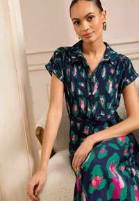 Abito navy con design a bottone, caratterizzato da una stampa astratta leopardata in rosa e verde, maniche corte e vita con cintura. Tessuto dalla texture liscia.