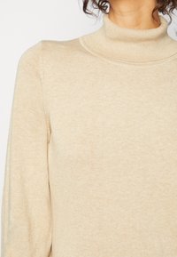 Beżowy sweter z golfem o miękkim, teksturowanym dzianinie. Posiada wysoki kołnierz i dopasowany krój, ukazując prostotę w designie.