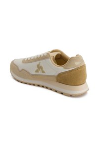 Sneaker beige e avorio con materiali in suede e pelle, punta rotonda, suola testurizzata e dettaglio del logo sul lato e sul tallone.