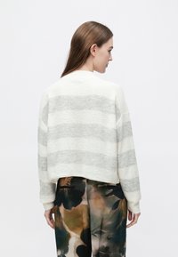 Pulover scurt cu dungi albe și gri, cu un finisaj texturat, cu umeri căzuți și decolteu rotund, asortat cu pantaloni cu model.