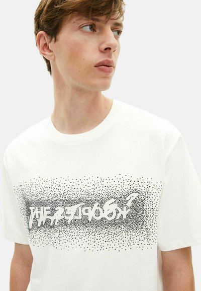 T-shirt branca de manga curta feita de algodão com decote redondo. Apresenta texto gráfico preto, salpicado, no peito.