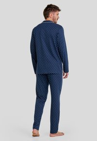 Conjunto de pijama en azul marino con puntos blancos, que incluye una camiseta de manga larga y pantalones con cinturilla elástica. Tela suave, ajuste relajado, sin acentos visibles.