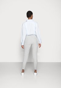 Chemise bleu clair à manches longues avec un col, associée à un pantalon gris clair à taille cintrée. La tenue est complétée par des baskets blanches.