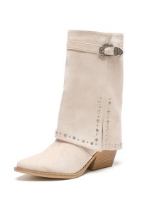 Botín de ante beige hasta el tobillo con puntera afilada, puño doblado, detalle de hebilla plateada y tachuelas a lo largo de la costura. Tacón de madera bajo.