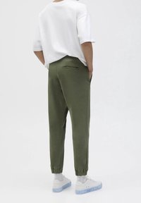 Pantalones jogger verde oliva con puños elásticos y un bolsillo trasero, combinados con una camiseta blanca de gran tamaño y zapatillas blancas con suela translúcida.