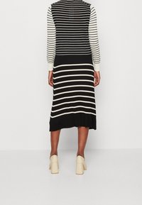 Schwarz-weiße gestreifte Midikleid mit langen Ärmeln, gerippter Textur und ausgestellt geschnittenem Saum. Trägt beigen Blockabsatzschuhe.