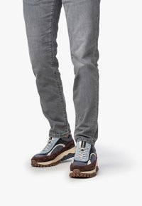 Sneakers z zaokrąglonym noskiem, z niebieską siateczką, brązowymi zamszowymi akcentami i białymi sznurowadłami. Gruba, teksturowana beżowa podeszwa zapewnia przyczepność.