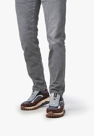 Baskets avec un bout arrondi, présentant un maillage bleu, des accents en daim marron et des lacets blancs. La semelle beige épaisse et texturée offre une bonne traction.