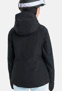 Black ski jacket with a hood, smooth texture, and adjustable features. The design includes a zippered back pocket, paired with gloves.