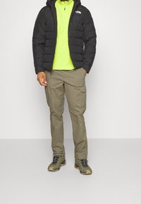 Musta puhvjakki, hehkuva vihreä vetoketjupaita, oliivinvihreät cargo-housut ja vihreät vaelluskengät. Huomionarvoisia piirteitä ovat taskut ja vetoketjut.