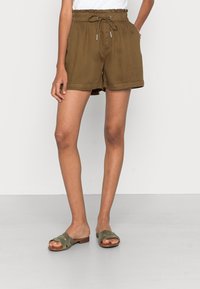Shorts marron avec cordon de serrage, à coupe décontractée, dotés d'une taille froncée et de revers repliés. Assortis avec des sandales à enfiler vertes.