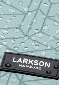 Voděodolná látka v mátové barvě s embosovaným geometrickým vzorem; obsahuje kapky a černou štítkovou nálepku s nápisem "LARKSON HAMBURG."